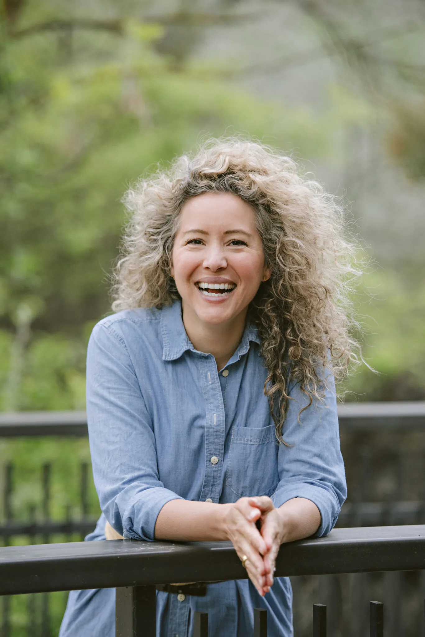 Smiling woman with curly hair in a blue shirt outdoors.