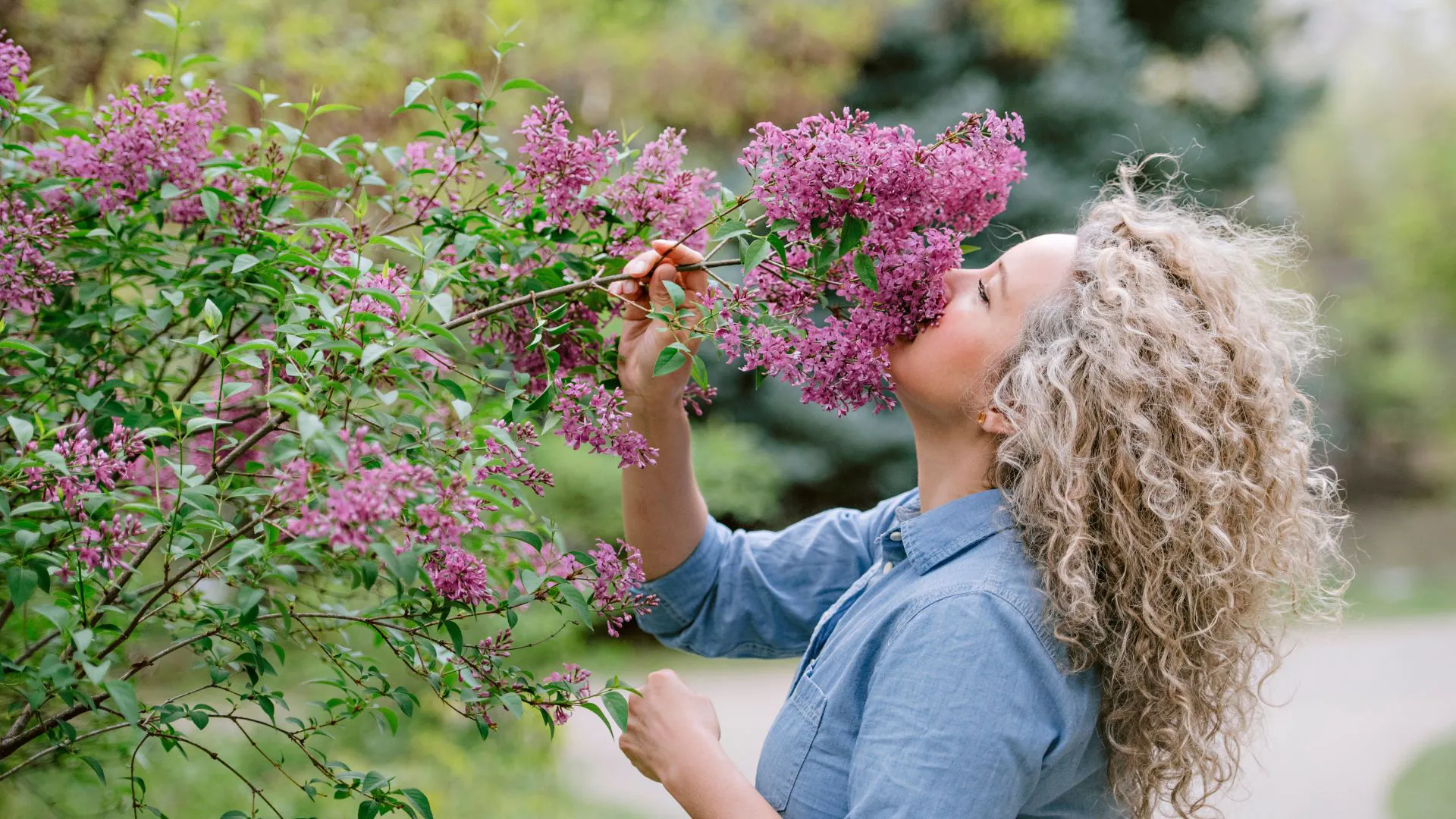 A woman smelling vibrant lilac flowers outdoors.