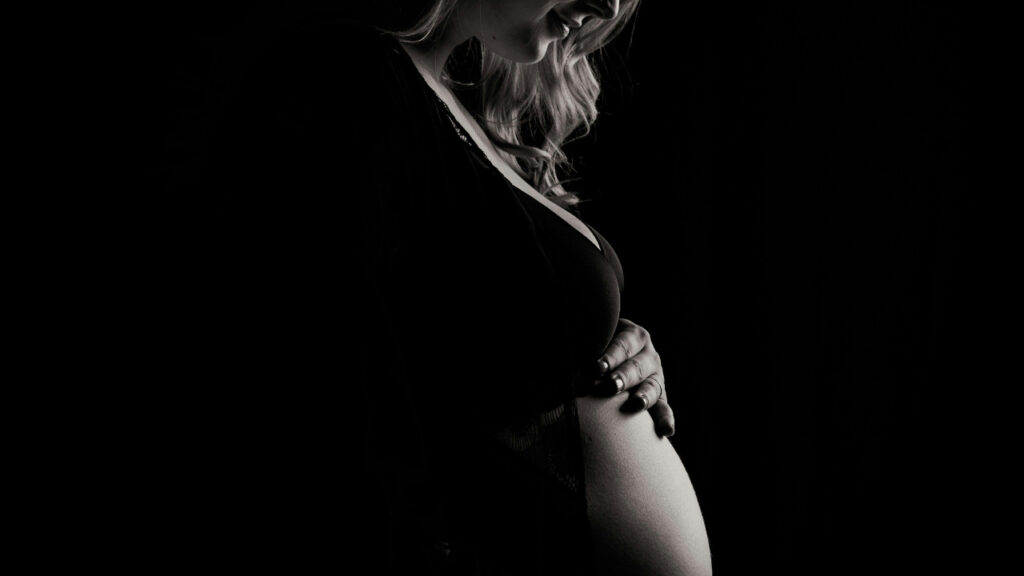 Silhouette of a pregnant woman gently holding her belly.