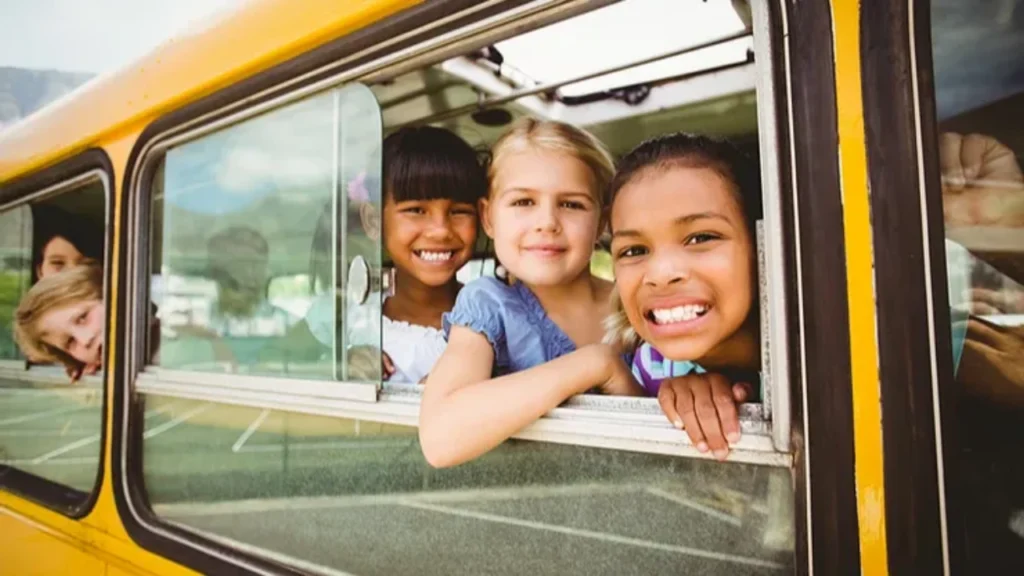 Three smiling girls looking out of a car window together.