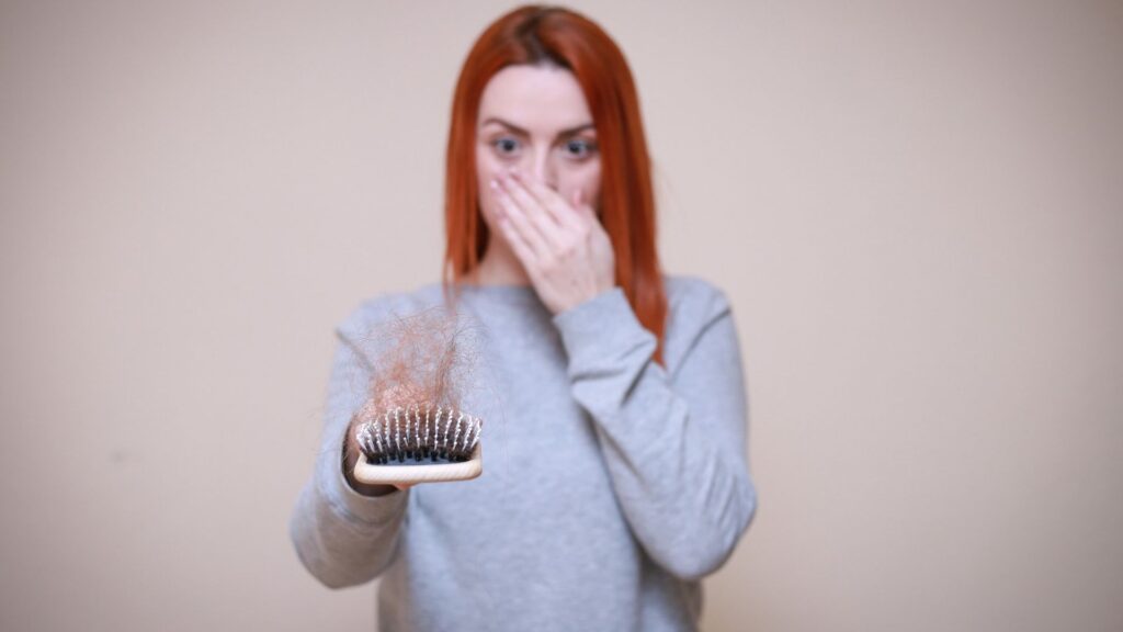 Woman holding a hairbrush with hair, covering her nose.