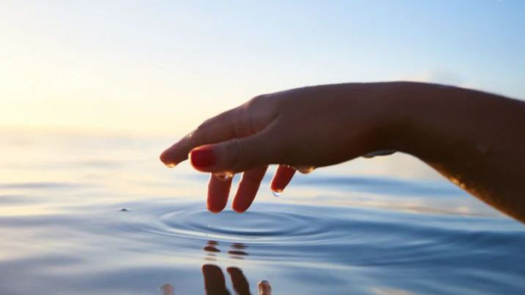 Hand gently touching calm water, creating soft ripples.