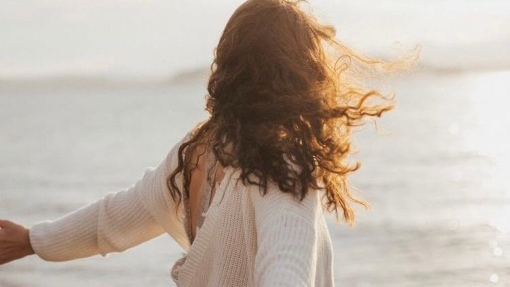 Woman with curly hair enjoying a windy beach moment.